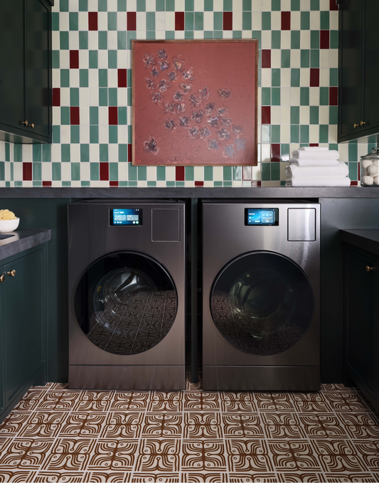 Pair of washing machines in a laundry room with decorative tiles and a painting on the wall.