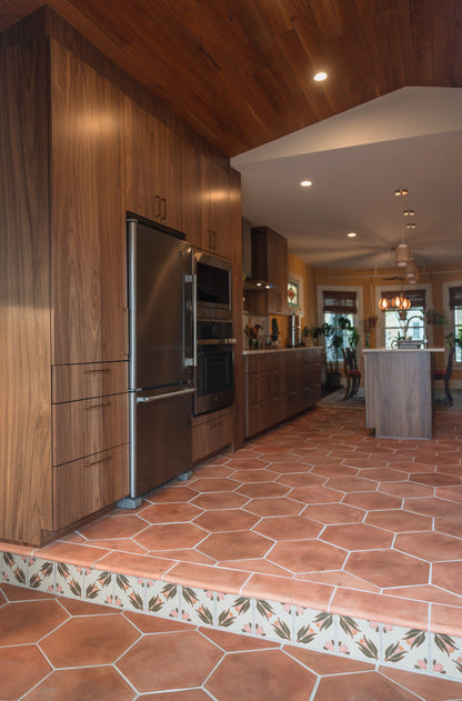 Modern kitchen with cotto terracotta hexagon floors, wooden cabinets, stainless steel appliances, and relief pattern riser tiles.