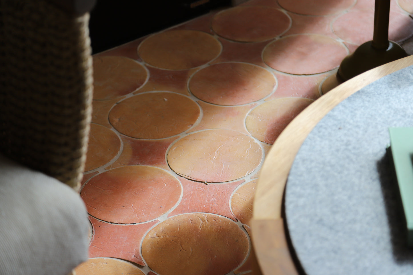 Close-up of a terracotta-colored oval tile floor with a pinkish-beige grout or joint line, partially framed by furniture in the foreground.