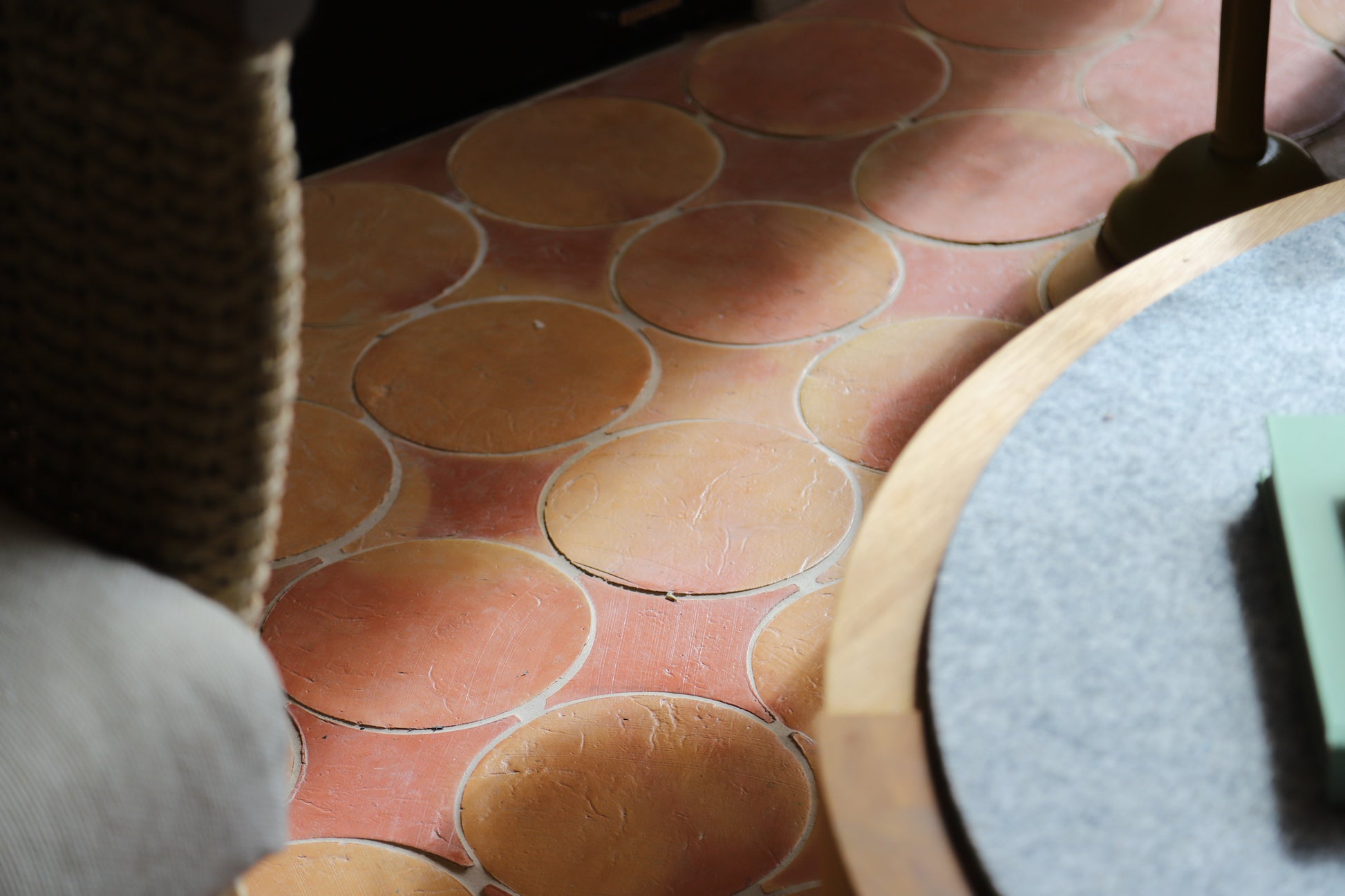 Close-up of a terracotta-colored oval tile floor with a pinkish-beige grout or joint line, partially framed by furniture in the foreground.
