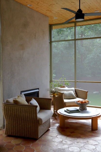 A cozy screened-in patio seating area with two woven wicker armchairs, a round wooden coffee table, and a textured stucco wall in the background.