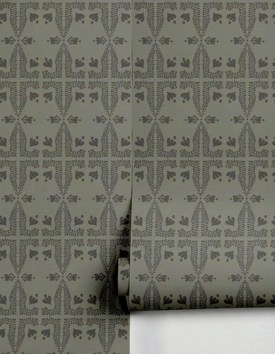 Sage green wallpaper by Clay Imports with a dark botanical pattern featuring symmetrical fern fronds and small leaf motifs, partially unrolled.