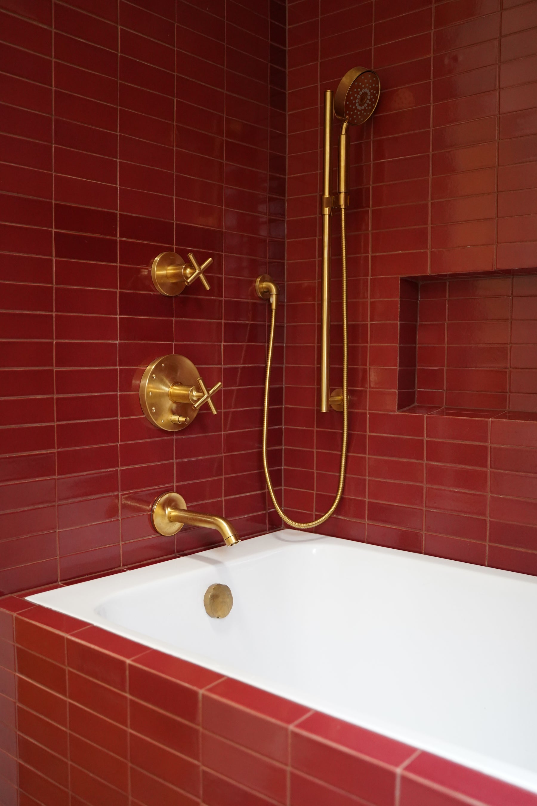 Plum 2x6 clay tiles by Clay Imports covering bathroom walls, with golden brass fixtures and a white bathtub.