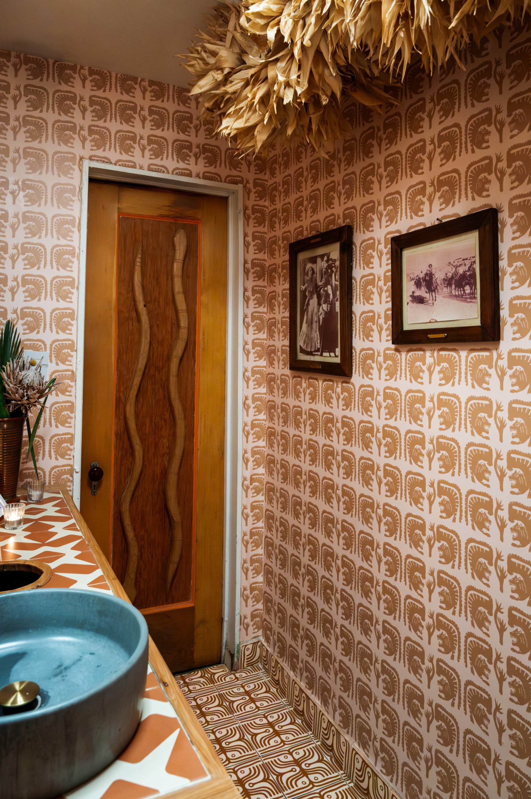 Small room with patterned wallpaper, wooden door, and framed pictures.