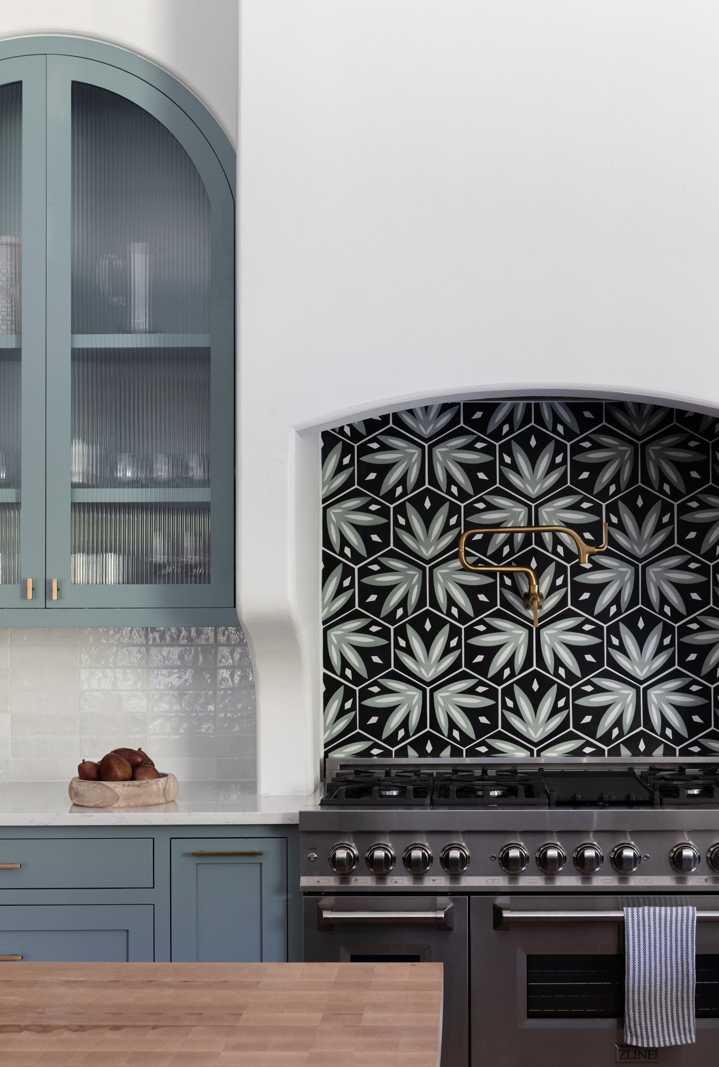 Tropicana Rucksack Green 8 pattern tile by Clay Imports, showcasing hexagonal green and white leaf designs on a black kitchen backsplash.