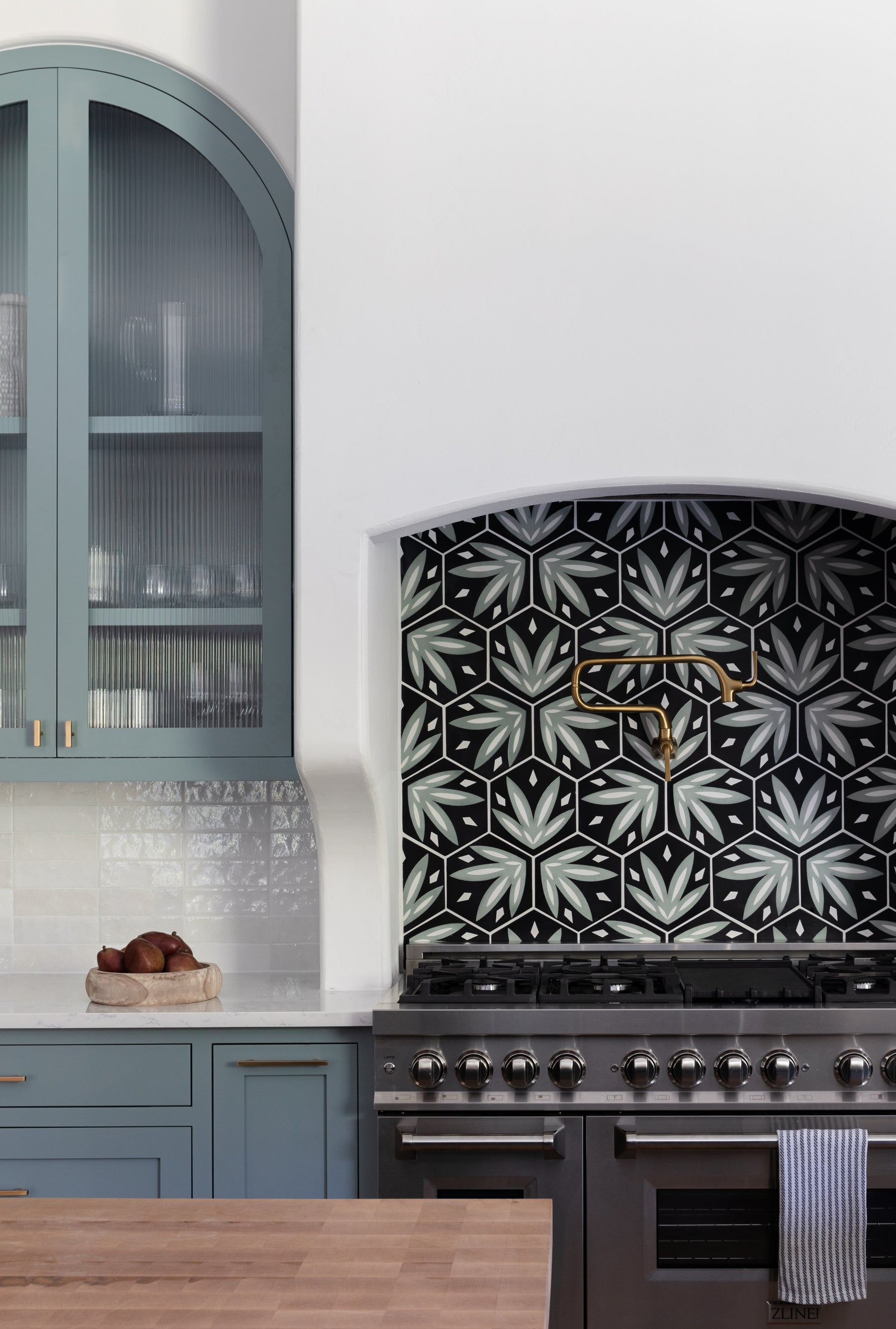 Tropicana Rucksack Green 8 pattern tile by Clay Imports, showcasing hexagonal green and white leaf designs on a black kitchen backsplash.