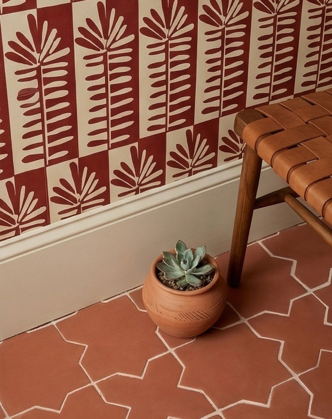 Terracotta Barro Star & Cross 6 solid tile by Clay Imports on a floor next to a succulent plant and woven leather bench.