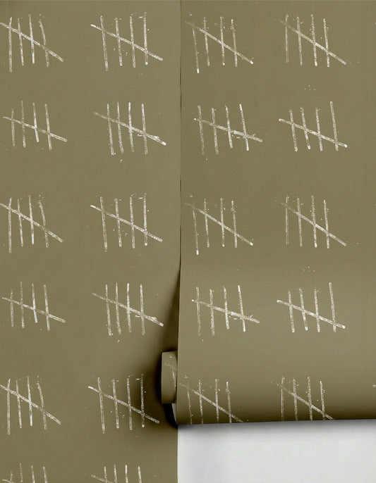 Muted olive green wallpaper by Clay Imports with a repeating pattern of distressed white tally marks, partially unrolled.