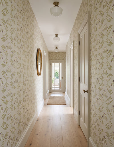 A long hallway with cream floral wallpaper, light wood floors, white doors, and ceiling light fixtures.
