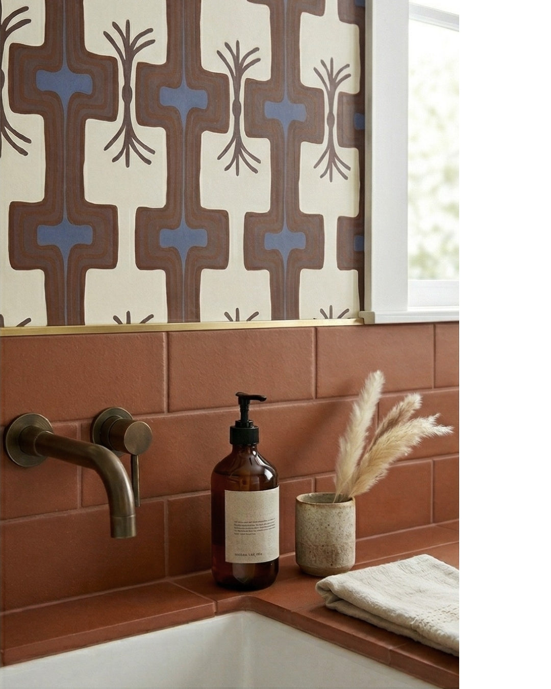 Cacao 2x6 solid tile by Clay Imports, reddish-brown subway tiles on a bathroom wall and counter with a brass faucet.