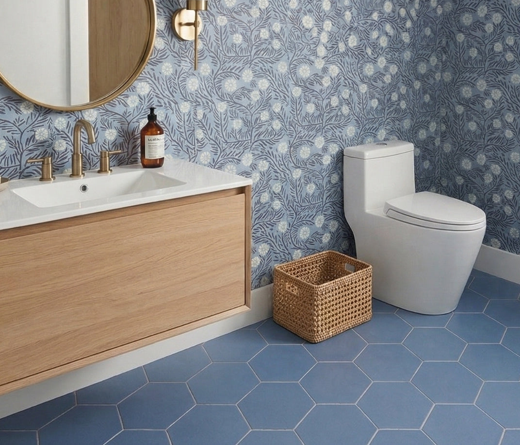 Blue hexagon clay floor tiles by Clay Imports installed in a bathroom with blue floral wallpaper and a wood vanity.