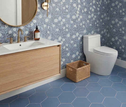 Blue hexagon clay floor tiles by Clay Imports installed in a bathroom with blue floral wallpaper and a wood vanity.