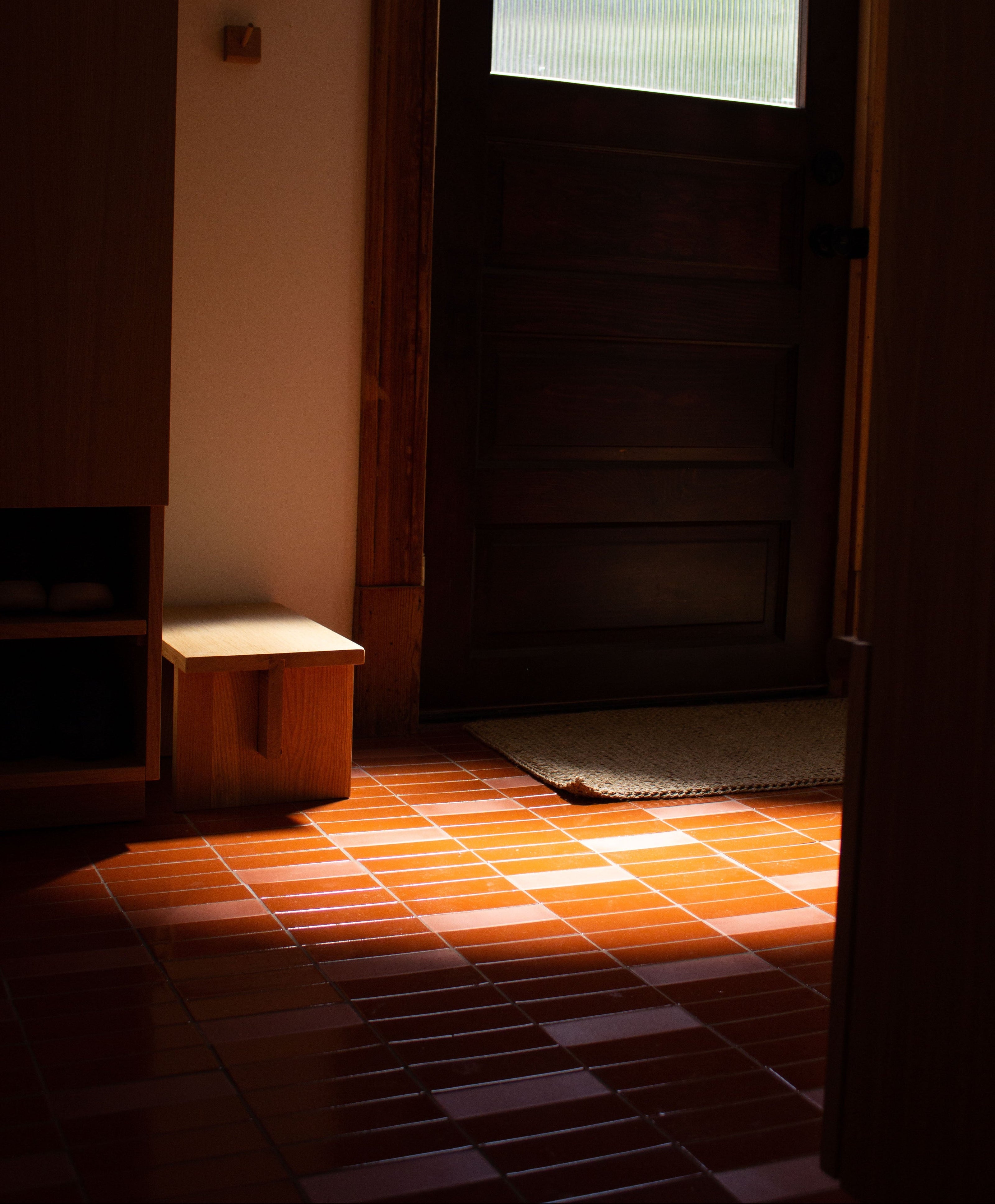 Whiskey 2x6 solid tile by Clay Imports, reddish-orange with a glossy finish, installed on a floor partially illuminated by sunlight.