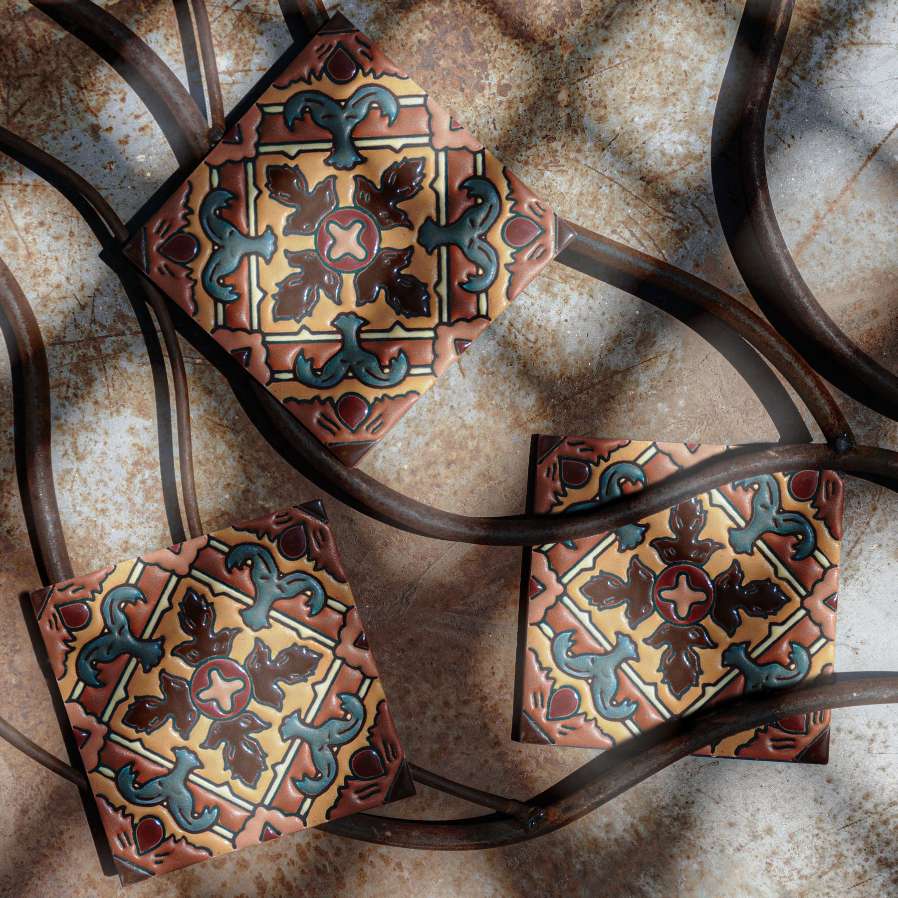 6x6 Relief Talavera tile by Clay Imports with ornate relief patterns in earthy tones, arranged on rustic metal with curved bars.