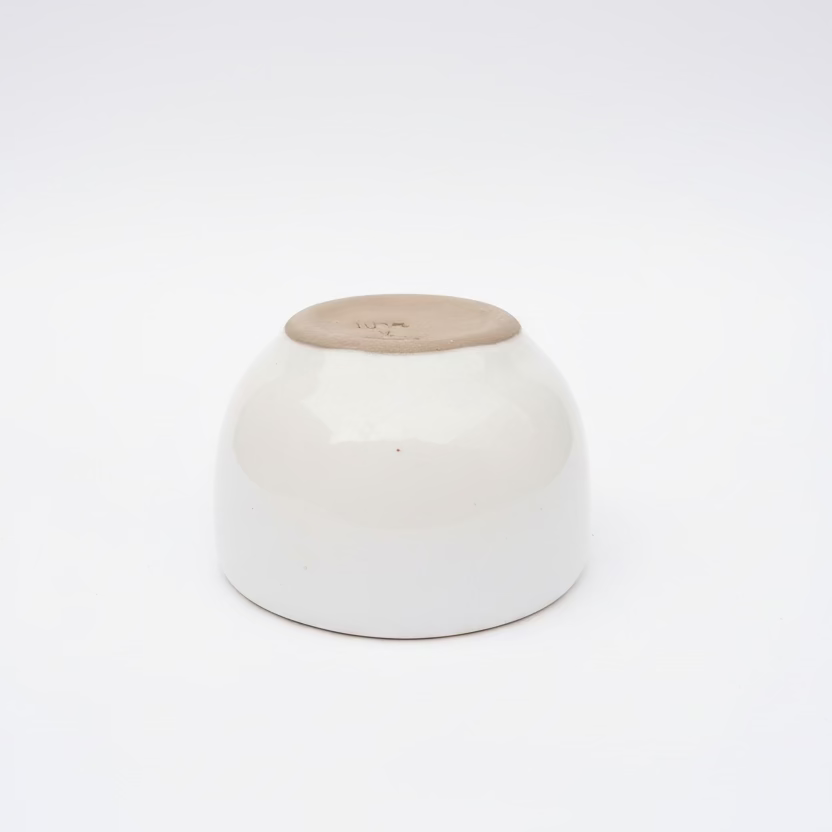 White gloss tea cup by Clay Imports with an exposed light brown rim, displayed upside down.