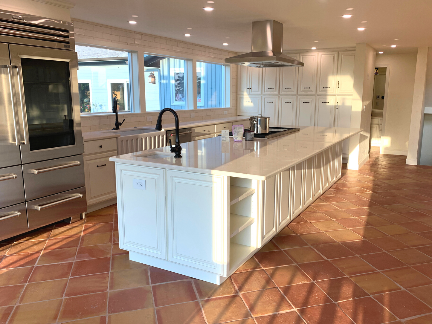 Antique satin terracotta tiles by Clay Imports in warm reddish-orange tones, forming a rustic kitchen floor reflecting sunlight.
