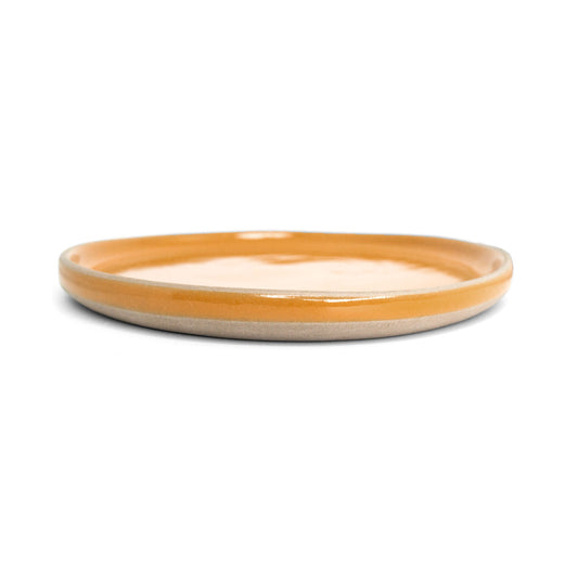 Orange ceramic dinner plate by Clay Imports with an unglazed beige rim, shown from the side.