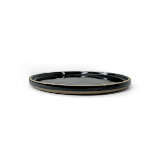 Snack plate with dark glaze and a visible unglazed clay rim by Clay Imports, viewed from the side.